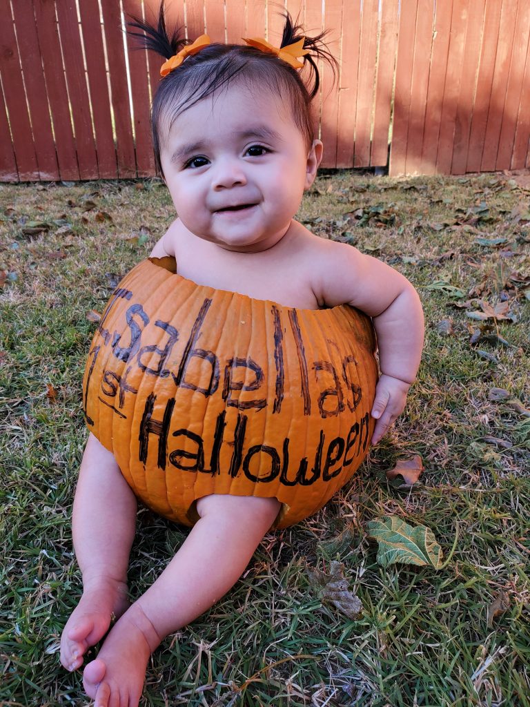 Photo of baby with orange hair bunches sitting in a carved out pumpkin in the garden