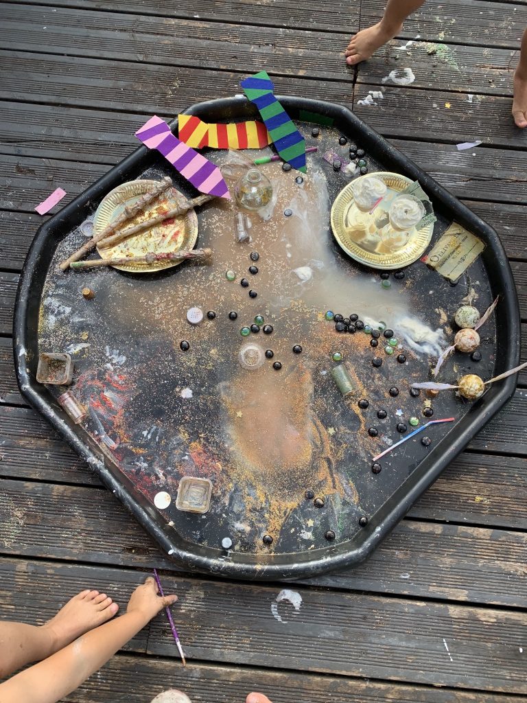 A photo of a tuff tray with lots of messy crafts  the photo also shows children's feet and hands. 