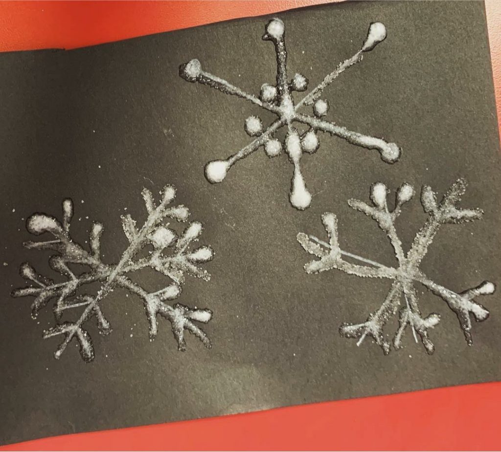 A photo of white sugar snowflakes on a black piece of card on a red background