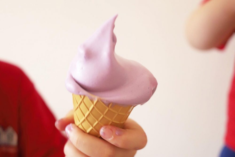 a photo of purple foam on a cone.  held by a childs hand 