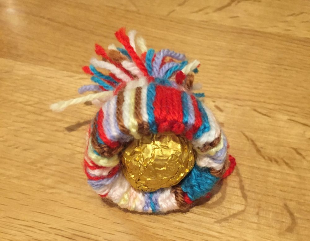 A photo of a colourful woolen hat christmas tree decoration. with a gold wrapper inside.