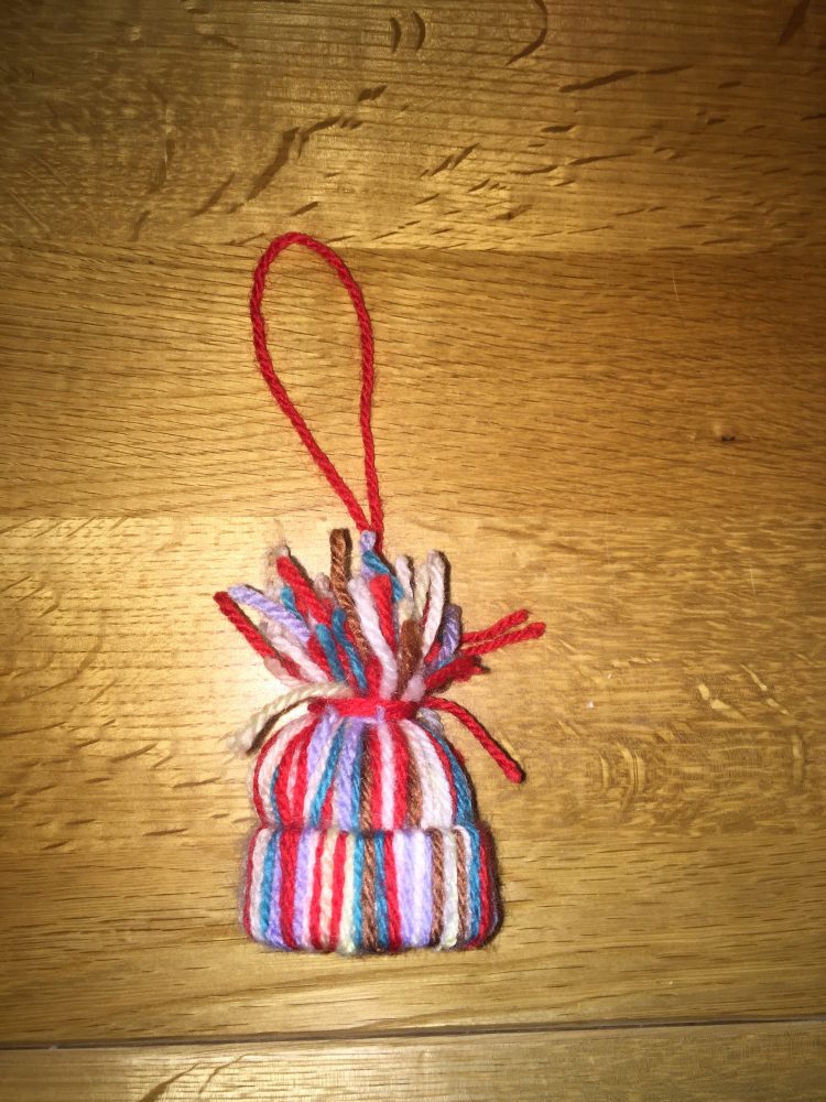 A photo of a colourful woolen hat christmas tree decoration.  on a brown wooden surface