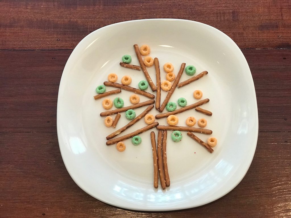 A photo of a plate with food (prezel sticks and hoops) on, shaped into a tree