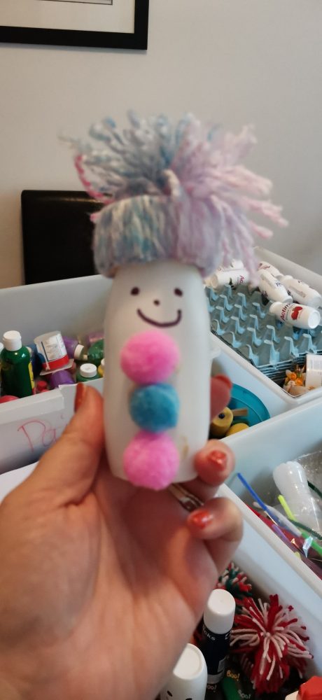 A photo of a woollen hat on a craft snowman with 3 pink and blue woollen balls and a smily face