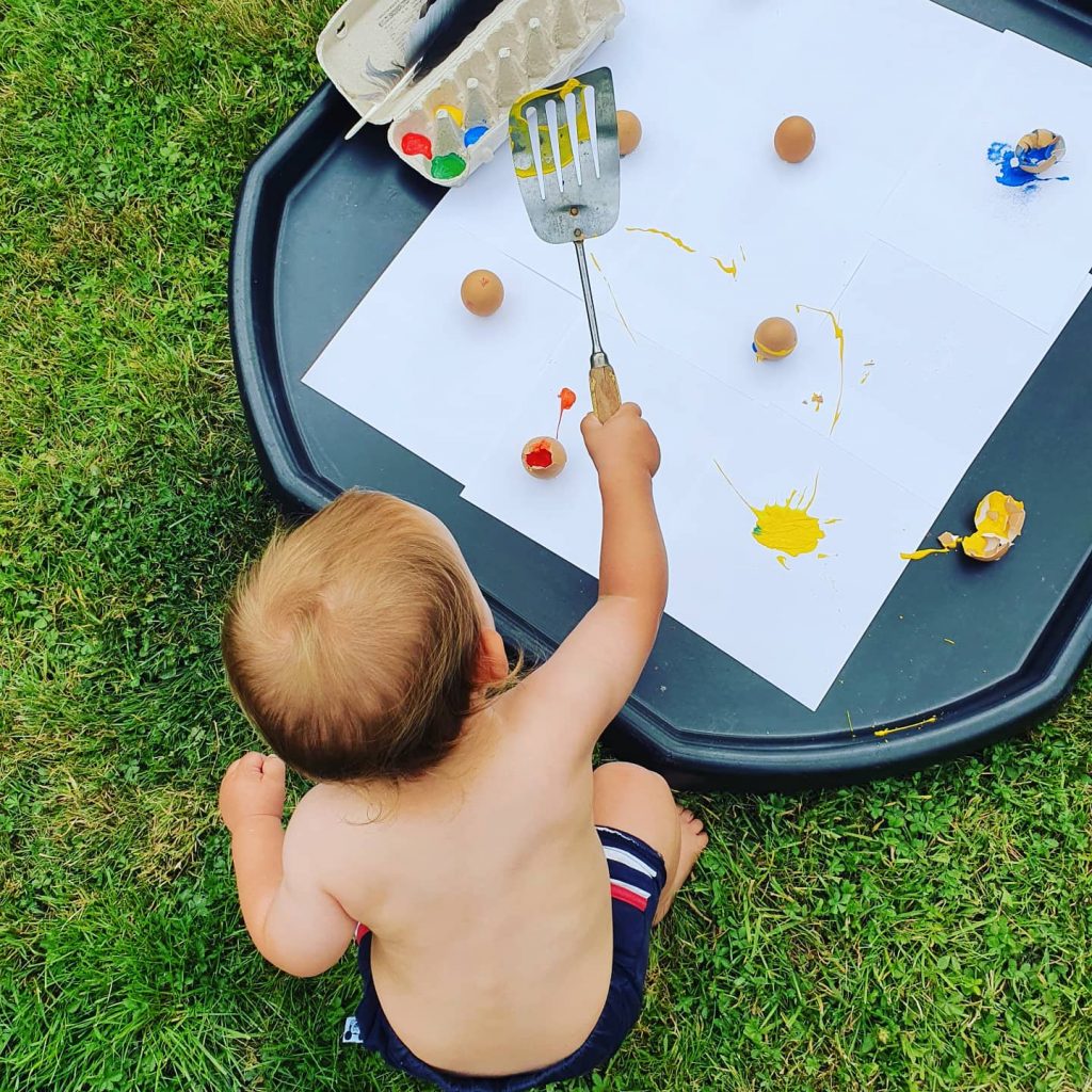 a photo of a child painting in the garden and holding a spatula.