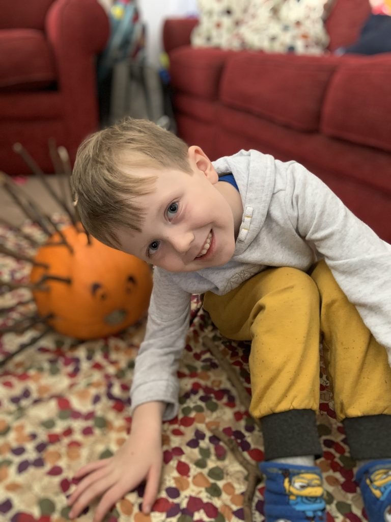 A photo of a boy smiling.  in the background there is a pumpkin with sticks in