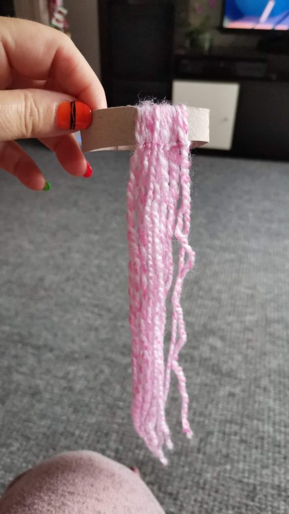 a photo of a hand holding cardboard with pink woollen strips hanging down