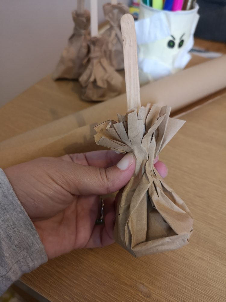 a photo of a hand holding a brown paper bag that looks like a witches broom