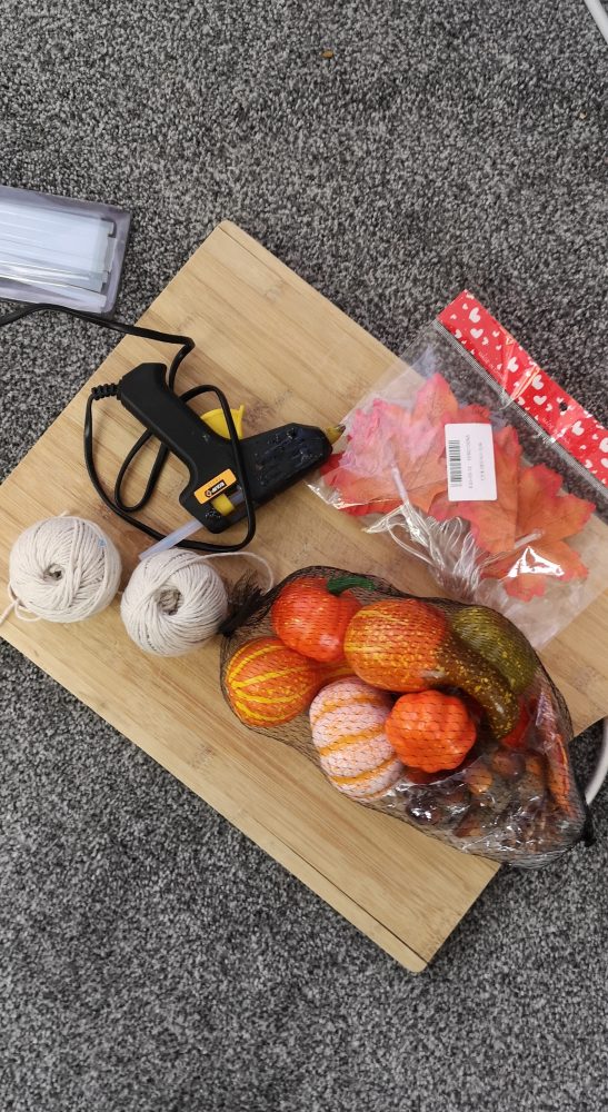 A photo of a glue gun, 2 balls of string, and autumn leaves and pumpkin decorations