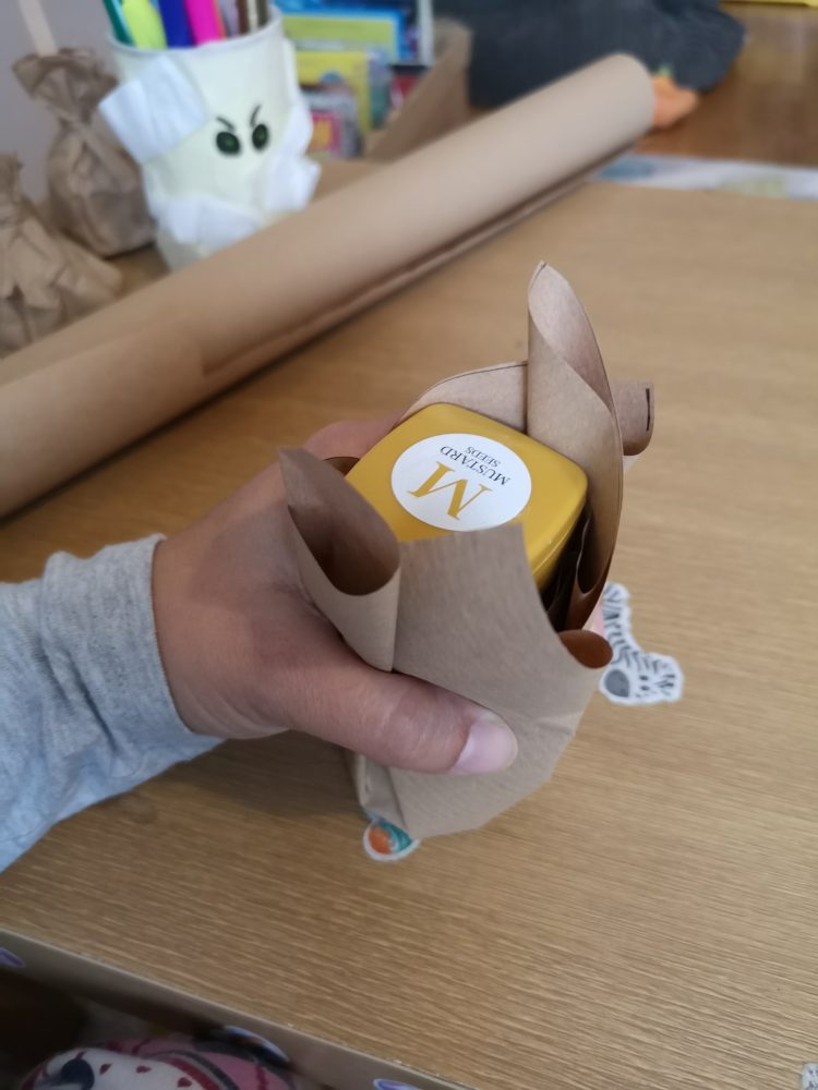 a photo of a hand holding brown paper around a container.