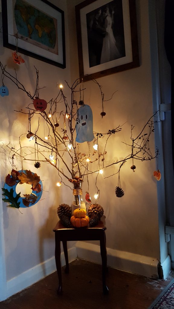 A photo of a twig tree with hanging halloween decorations - a ghost, pumpkins, pinecones, leaves. on a table 