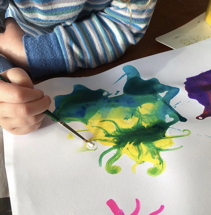 White paper with colourful paint splats on them.  a childs hand is painting. 