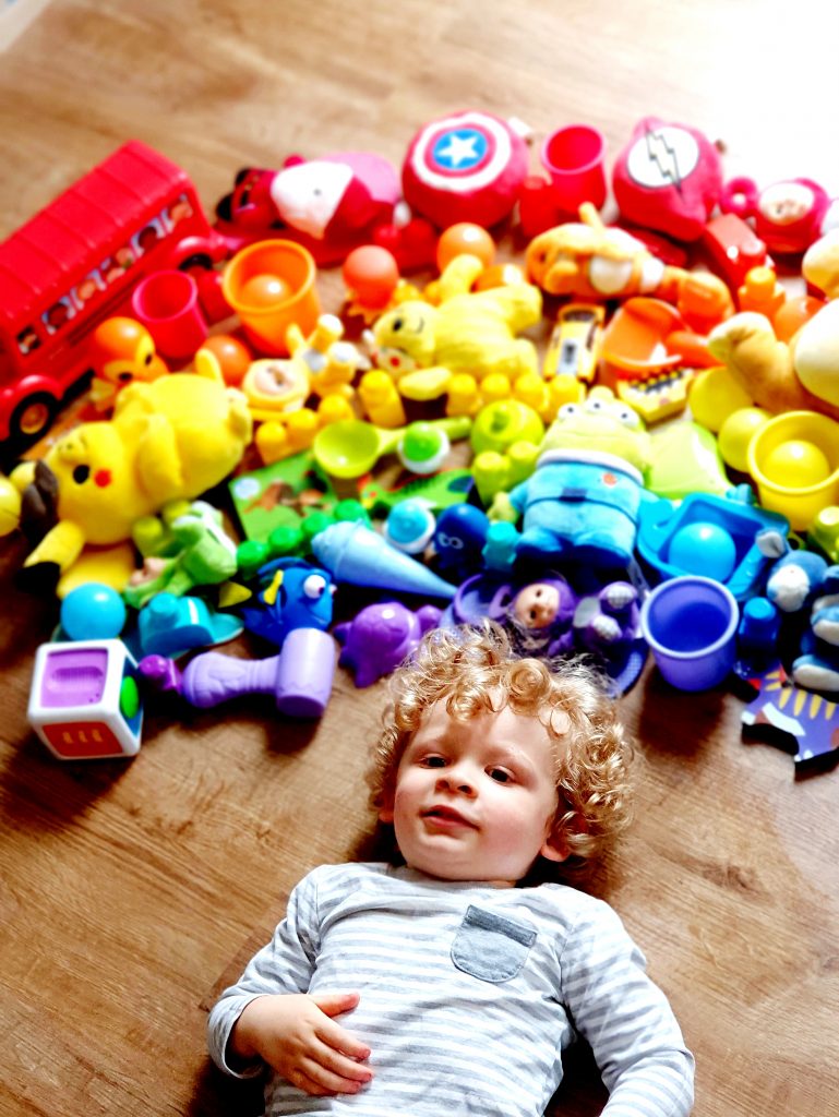 A photo of a young child laying on the ground.  Above him are a rainbow of coloured toys