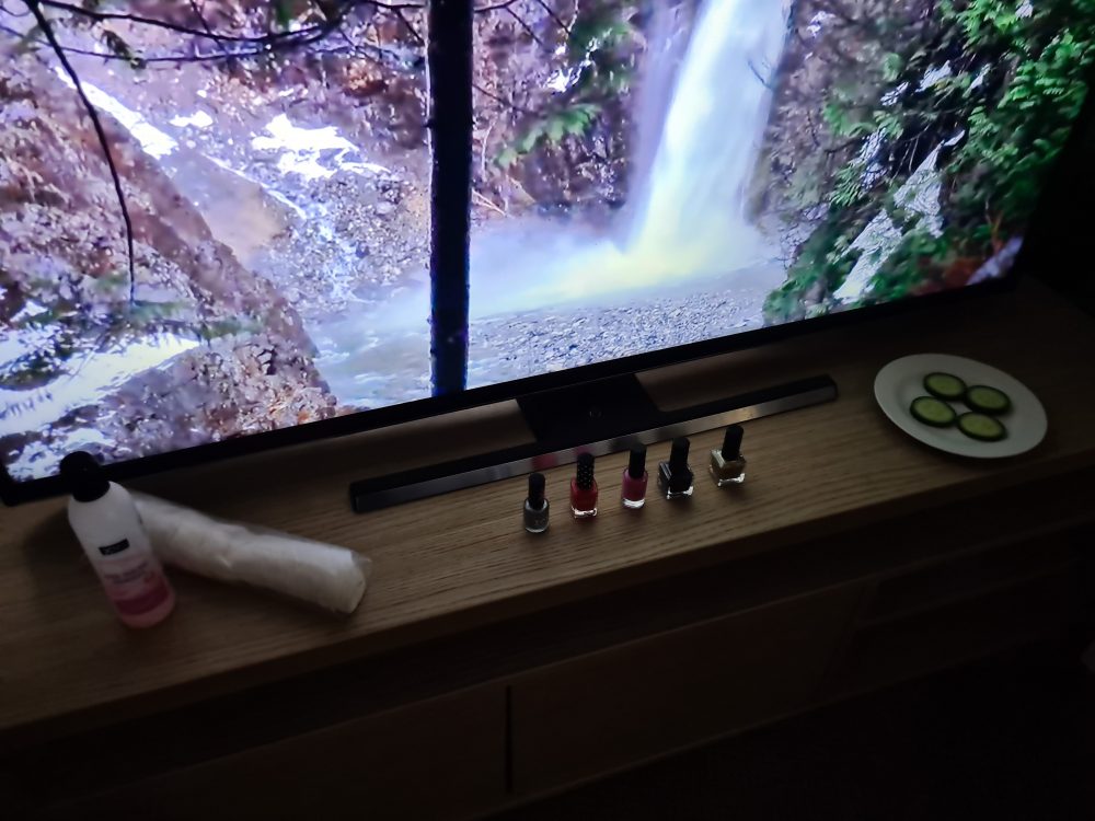 A photo of a screen with a waterfall on, nail varnish remover, 5 nail varnishes and a plate with green cucumber slices on