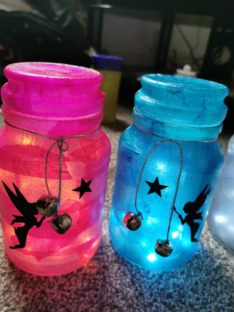 A photo of a pink jar and a blue jar, both have pictures of a fairy, a star and some bells on