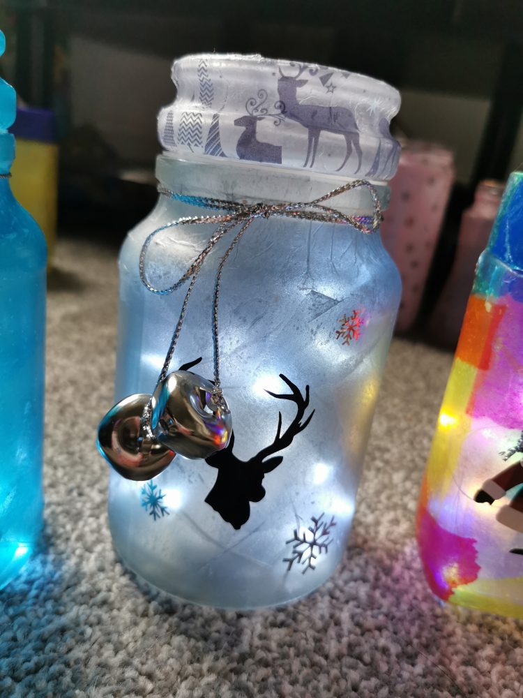 A photo of a jar it has a stags head and snowflakes images on. and some bells on