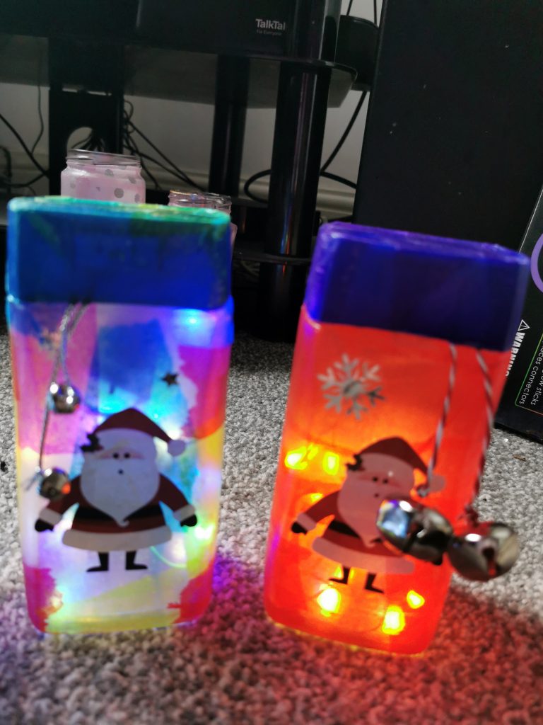 A photo of 2  jars, both have pictures of father christmas  and some bells on