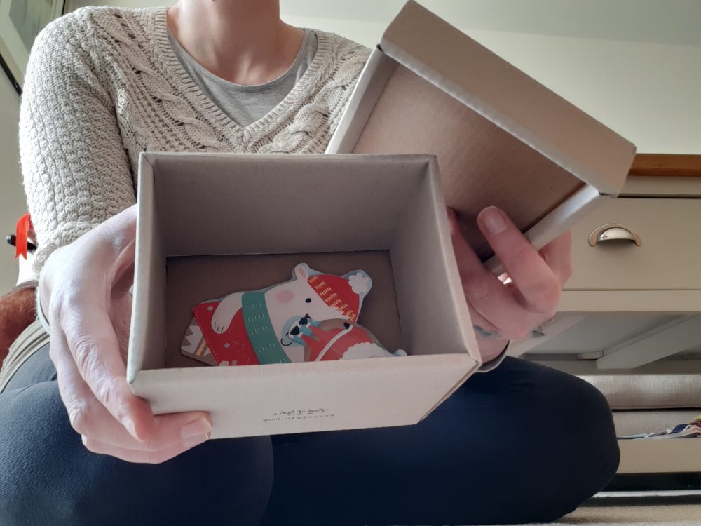 A photo of a woman holding a cardboard box to camera showing paper pictures inside.