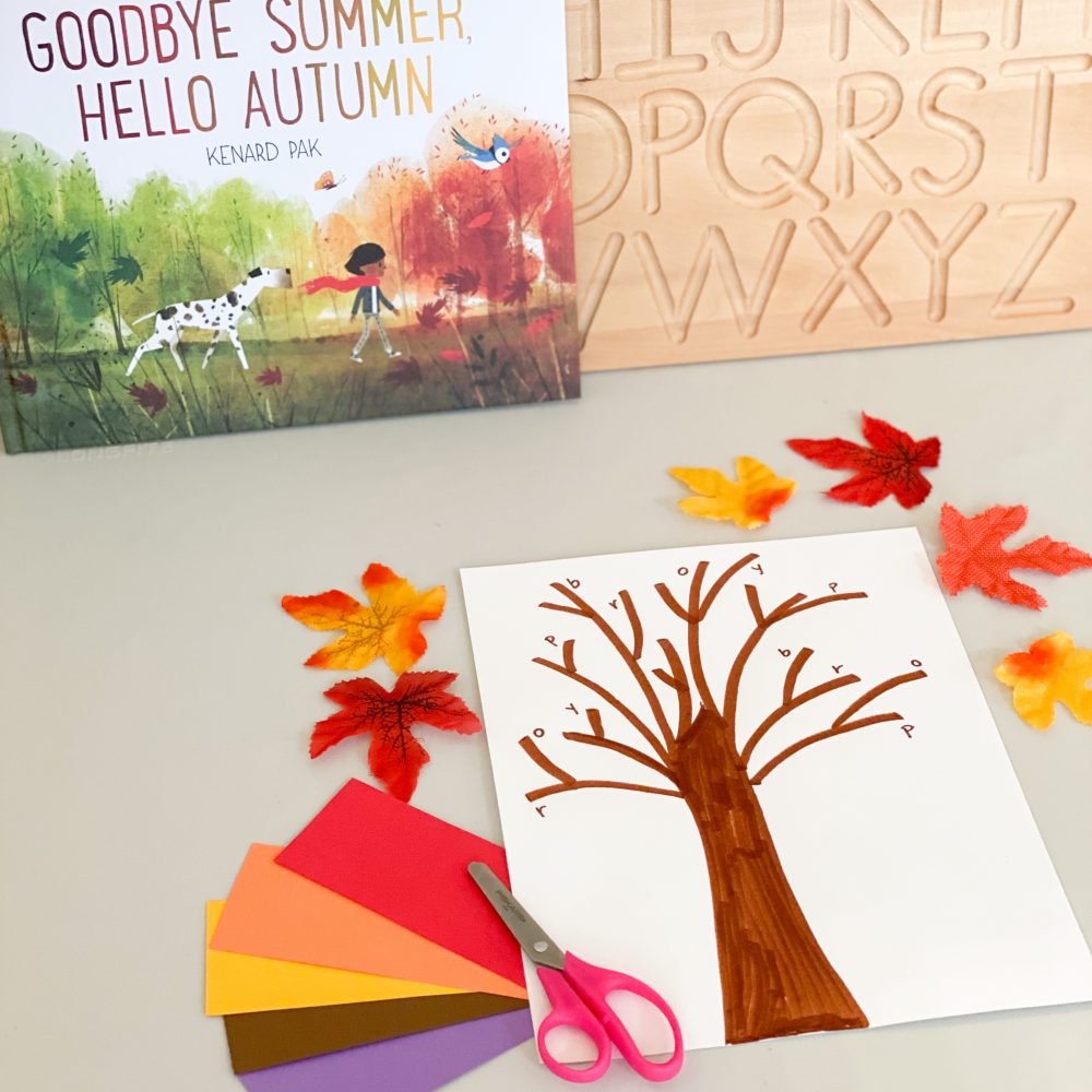 A photo of a book and a piece of paper with a tree drawn on, there is also pink scissors, coloured paper and autumn colour leaves